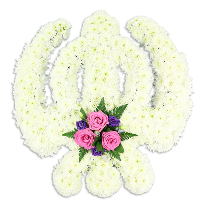 A reverent floral interpretation of the Sikh Khanda symbol is presented in front of a spotless white background, its strong, recognisable outline shaped entirely from tightly packed white chrysanthemum florets. The florist has built the emblem with sculptural care: the rounded chakkar ring forms a smooth halo; within it, the central double-edged sword rises straight and true; and on either side, the two kirpans sweep outward in balanced arcs, their tips meeting the lower curve to complete the sacred form. The chrysanthemums, chosen in shades of pure white and soft cream, create a uniform, cloud-like texture, with each individual bloom adding to a sense of purity and devotion often associated with Sikh funeral tributes across South Norwood. At the base, where the blades converge, a smaller accent arrangement draws the eye. Three rich pink roses, fresh and velvety, sit at the heart of this cluster, their petals slightly cupped as if holding unspoken words of farewell. Around them, intricate deep purple flowers - likely lisianthus or delicate freesias - thread through the design, introducing a dignified depth of colour. Wisps of dark green fern and glossy foliage weave between the petals, creating a subtle frame that enhances the central blooms without distracting from the white Khanda. The entire piece is lit evenly, with a faint shadow below that lends a quiet three-dimensional quality, as though the emblem gently rises from the surface. This style of tribute would be chosen by South Norwood families seeking to honour a loved one's Sikh faith with something both traditional and beautifully handcrafted, a floral expression of respect, remembrance, and spiritual continuity.